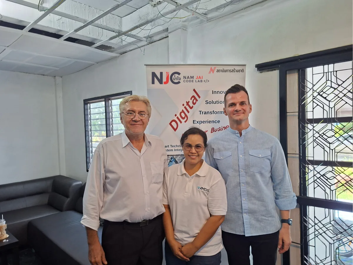Prof. Dr.-Ing. Norman Hoeltz visiting the Nam Jai Code Lab with Dr. Roland Petrasch and Mrs. Sudarat, standing in front of the NJCL banner